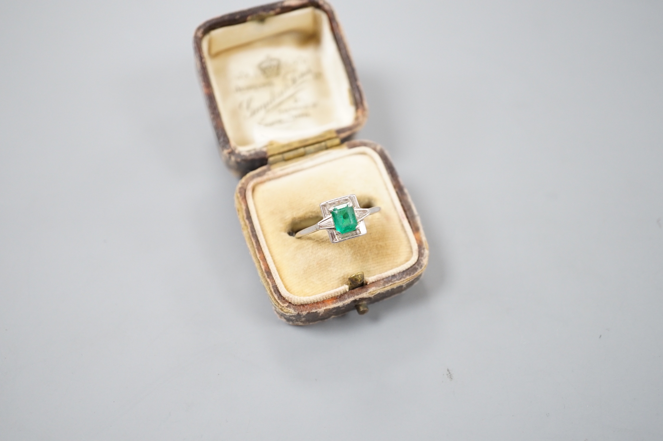 An Art Deco white metal, single stone emerald, baguette and trapeze cut diamond cluster set ring, size R/S, gross 3.5 grams